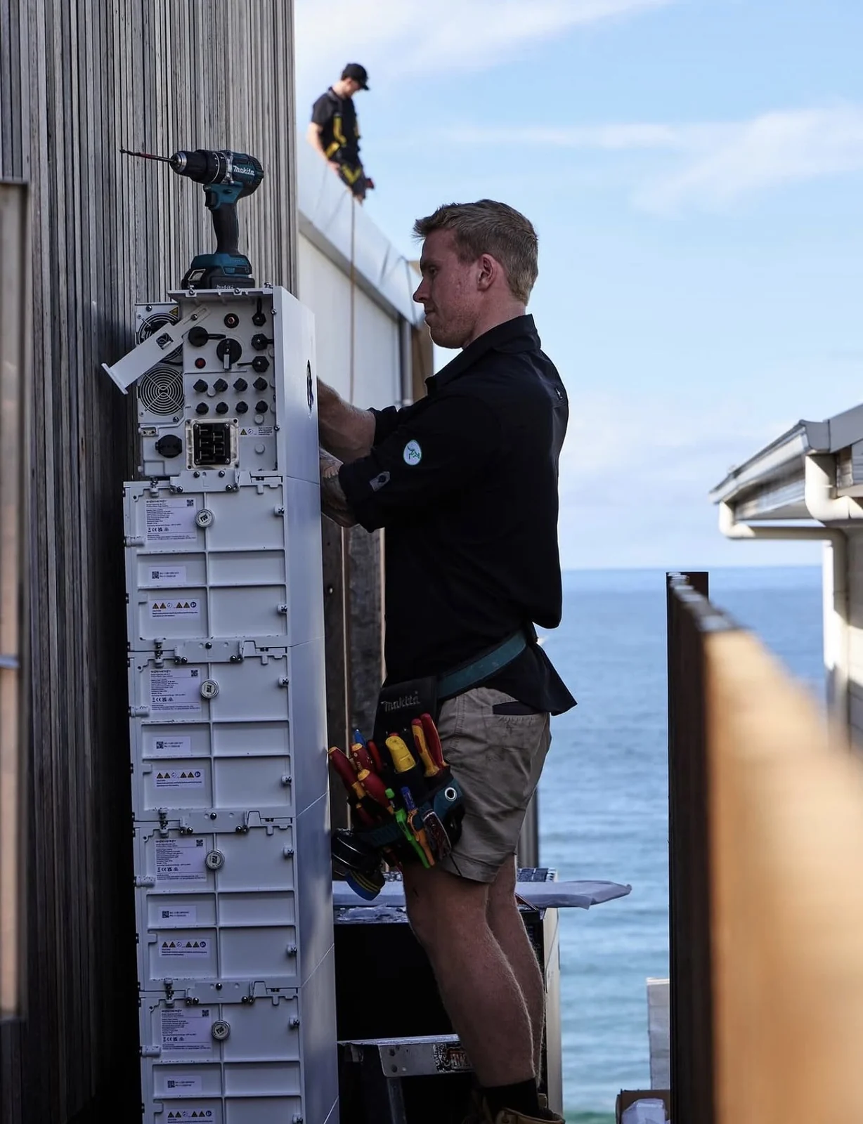 Ausave installer fitting a battery system with ocean views